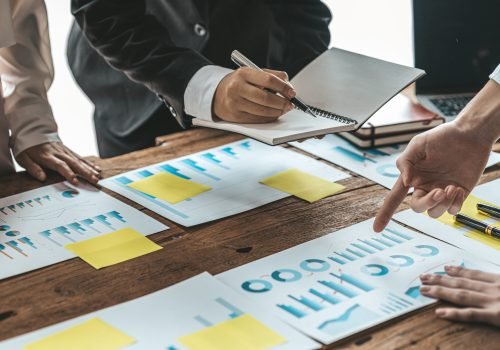 A desk in a company conference room has a group of business people attending and with supporting documents laid out, brainstorming sessions to fix and plan the company's growth. Business meeting idea.